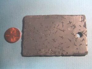 A lead coupon shows evidence of cavitation erosion after several hours exposure to ultrasonic energy in water.